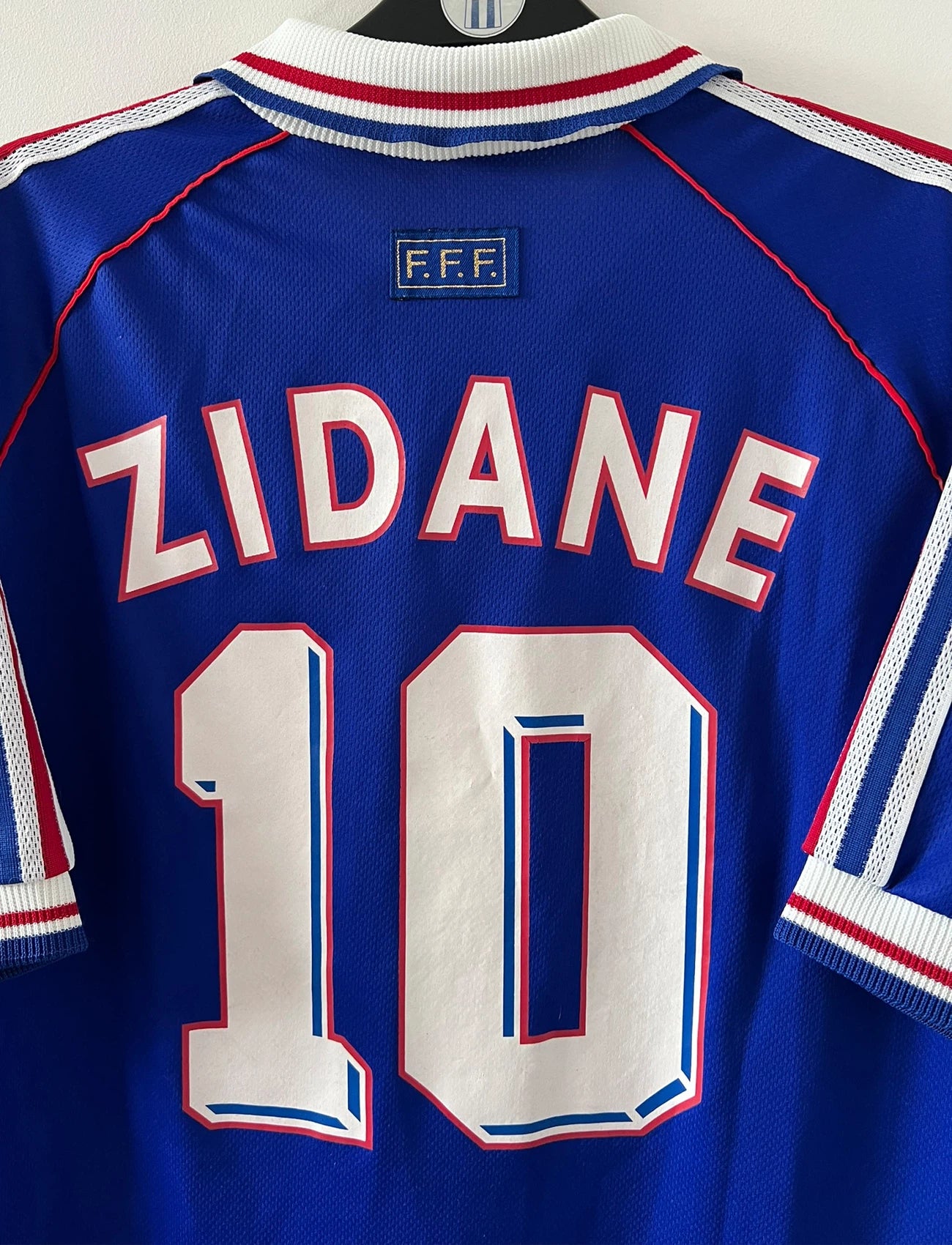 Maillot de foot vintage domicile bleu de l'équipe de france 1998. On peut retrouver l'équipementier Adidas. Le maillot est floqué du numéro 10 Zinedine Zidane. Il s'agit d'un maillot authentique d'époque.