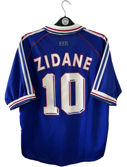 Maillot de foot vintage domicile bleu de l'équipe de france 1998. On peut retrouver l'équipementier Adidas. Le maillot est floqué du numéro 10 Zinedine Zidane. Il s'agit d'un maillot authentique d'époque.