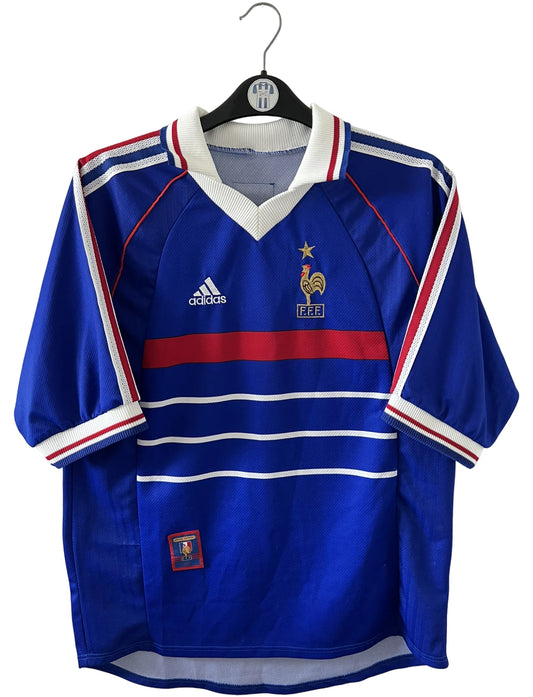 Maillot de foot vintage domicile bleu de l'équipe de france 1998. On peut retrouver l'équipementier Adidas. Le maillot est floqué du numéro 10 Zinedine Zidane. Il s'agit d'un maillot authentique d'époque.