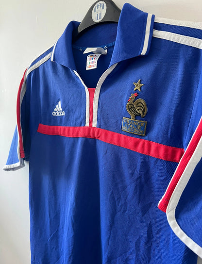 Maillot de foot vintage domicile bleu de l'équipe de france 2000. On peut retrouver l'équipementier Adidas et le flocage de Zinedine Zidane. Il s'agit d'un maillot authentique d'époque.