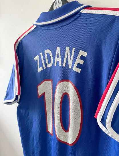Maillot de foot vintage domicile bleu de l'équipe de france 2000. On peut retrouver l'équipementier Adidas et le flocage de Zinedine Zidane. Il s'agit d'un maillot authentique d'époque.