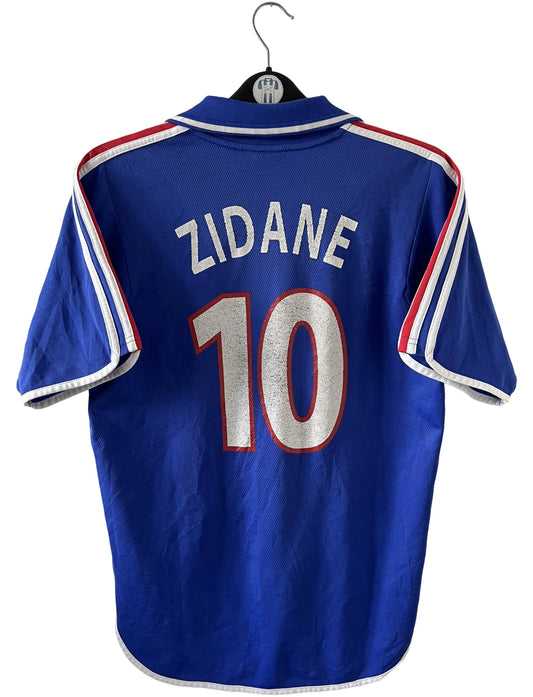 Maillot de foot vintage domicile bleu de l'équipe de france 2000. On peut retrouver l'équipementier Adidas et le flocage de Zinedine Zidane. Il s'agit d'un maillot authentique d'époque.