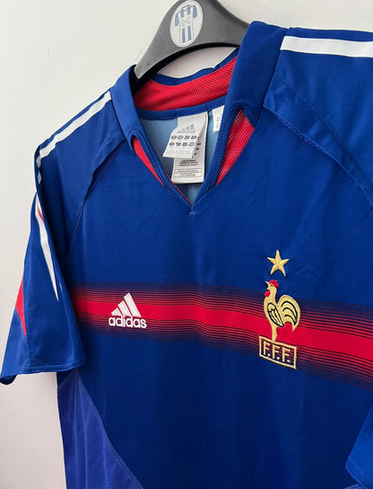 Maillot de foot vintage domicile bleu de l'équipe de france 2004. On peut retrouver l'équipementier Adidas. Le maillot est floqué du numéro 10 Zinedine Zidane. Il s'agit d'un maillot authentique d'époque.