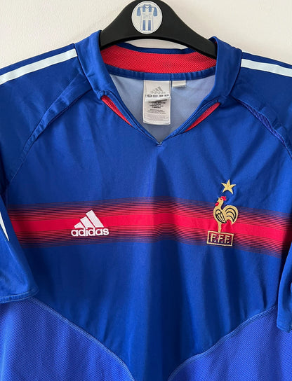 Maillot de foot vintage domicile bleu de l'Equipe de France 2004. On peut retrouver l'équipementier Adidas. Le maillot est floqué du numéro 10 Zinedine Zidane. Il s'agit d'un maillot authentique d'époque.