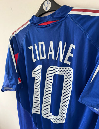 Maillot de foot vintage domicile bleu de l'Equipe de France 2004. On peut retrouver l'équipementier Adidas. Le maillot est floqué du numéro 10 Zinedine Zidane. Il s'agit d'un maillot authentique d'époque.
