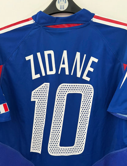 Maillot de foot vintage domicile bleu de l'équipe de france 2004. On peut retrouver l'équipementier Adidas. Le maillot est floqué du numéro 10 Zinedine Zidane. Il s'agit d'un maillot authentique d'époque.