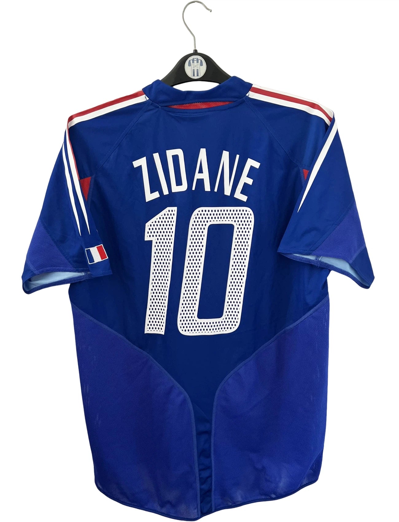 Maillot de foot vintage domicile bleu de l'équipe de france 2004. On peut retrouver l'équipementier Adidas. Le maillot est floqué du numéro 10 Zinedine Zidane. Il s'agit d'un maillot authentique d'époque.