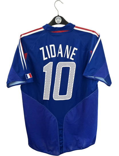 Maillot de foot vintage domicile bleu de l'équipe de france 2004. On peut retrouver l'équipementier Adidas. Le maillot est floqué du numéro 10 Zinedine Zidane. Il s'agit d'un maillot authentique d'époque.