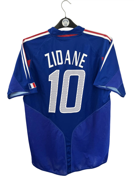 Maillot de foot vintage domicile bleu de l'équipe de france 2004. On peut retrouver l'équipementier Adidas. Le maillot est floqué du numéro 10 Zinedine Zidane. Il s'agit d'un maillot authentique d'époque.