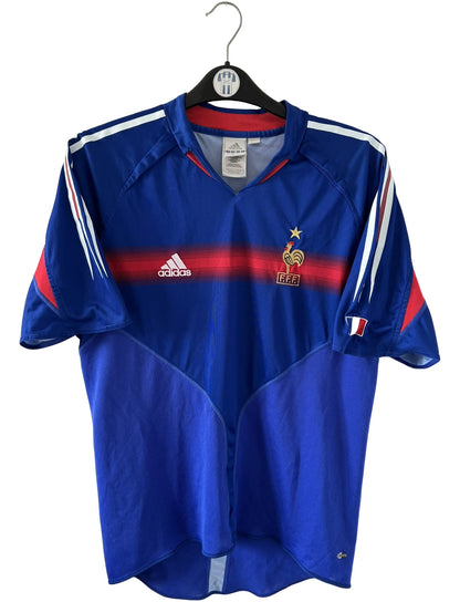 Maillot de foot vintage domicile bleu de l'Equipe de France 2004. On peut retrouver l'équipementier Adidas. Le maillot est floqué du numéro 10 Zinedine Zidane. Il s'agit d'un maillot authentique d'époque.