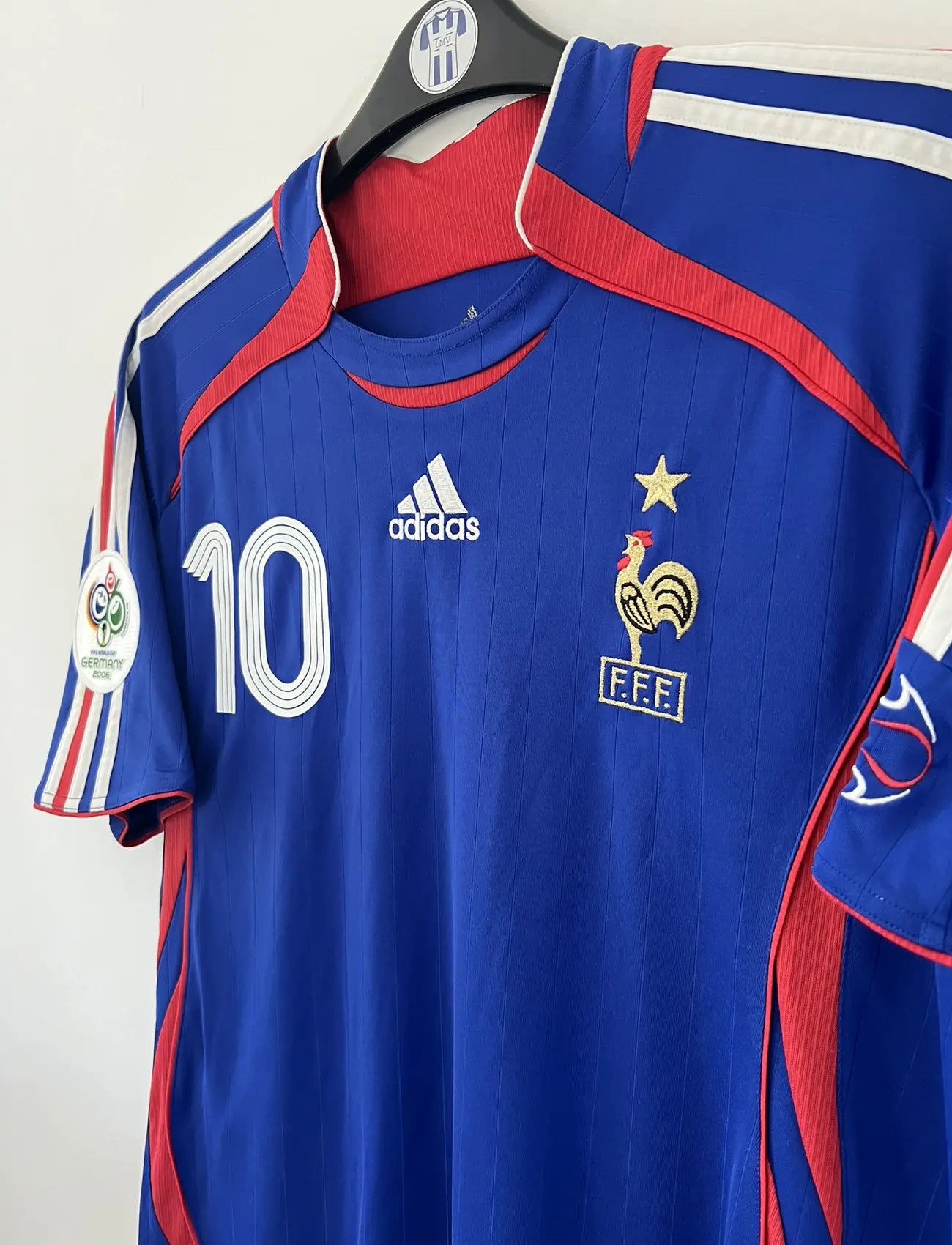 Maillot de foot vintage domicile bleu, blanc et rouge de l'équipe de france 2006. On peut retrouver l'équipementier adidas. Le maillot est floqué du numéro 10 Zinedine Zidane. Il s'agit d'un maillot authentique d'époque comportant l'étiquette 740126