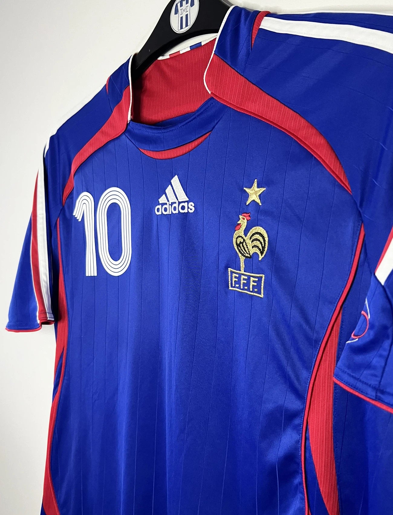 Maillot de foot vintage domicile bleu de l'équipe de france 2006. On peut retrouver l'équipementier Adidas. Le maillot est floqué du numéro 10 Zinedine Zidane. Il s'agit d'un maillot authentique d'époque comportant l'étiquette 740126.