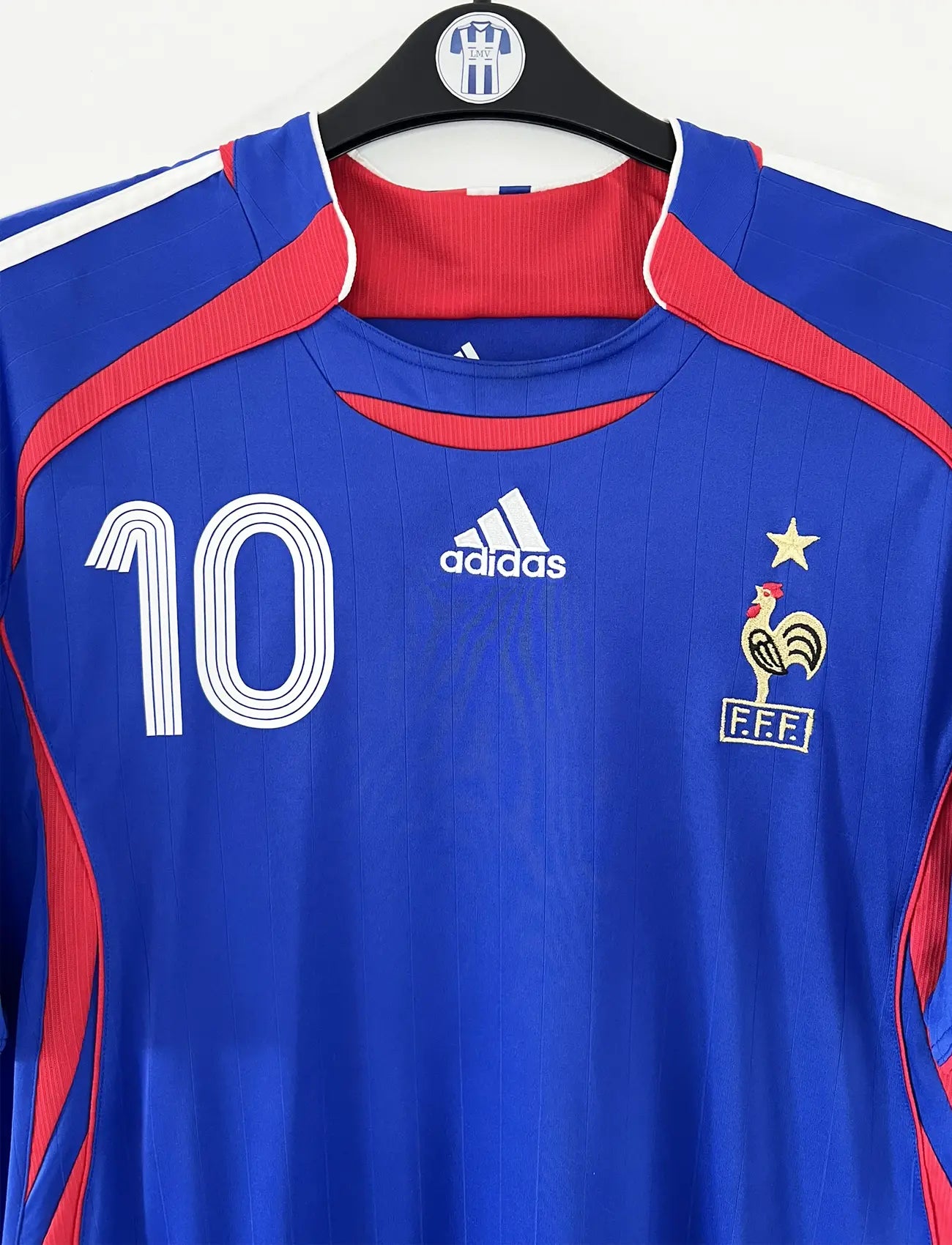 Maillot de foot vintage domicile bleu, blanc et rouge de l'équipe de france 2006. On peut retrouver l'équipementier adidas. Le maillot est floqué du numéro 10 Zinedine Zidane. Il s'agit d'un maillot authentique d'époque comportant l'étiquette 740126. Le maillot est un taille XL
