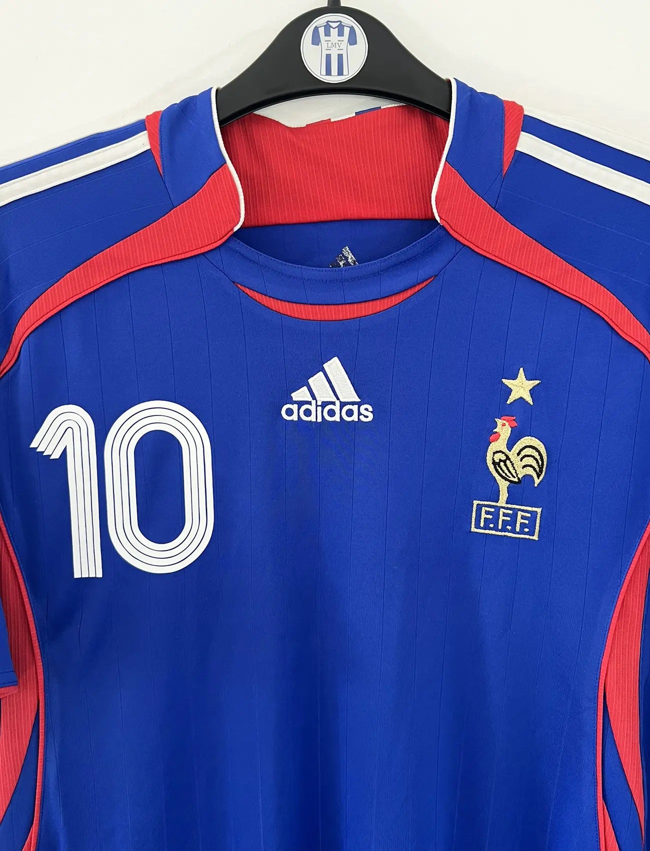 Maillot de foot vintage domicile bleu, blanc et rouge de l'équipe de france 2006. On peut retrouver l'équipementier adidas. Le maillot est floqué du numéro 10 Zinedine Zidane. Il s'agit d'un maillot authentique d'époque comportant l'étiquette 740126