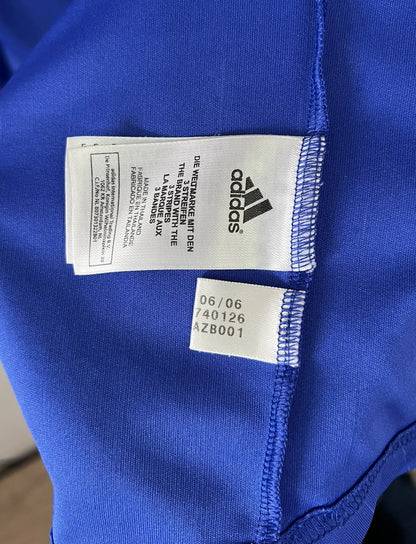 Maillot de foot vintage domicile bleu, blanc et rouge de l'équipe de france 2006. On peut retrouver l'équipementier adidas. Le maillot est floqué du numéro 10 Zinedine Zidane. Il s'agit d'un maillot authentique d'époque comportant l'étiquette 740126. Le maillot est un taille XL