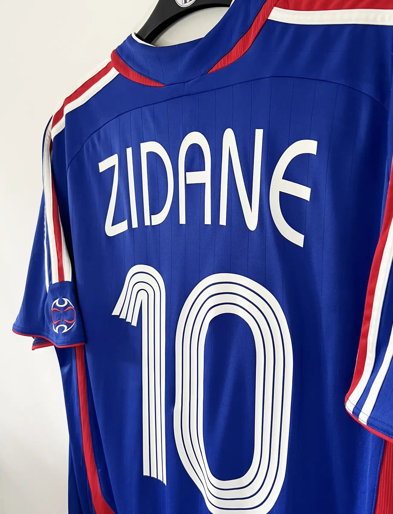Maillot de foot vintage domicile bleu, blanc et rouge de l'équipe de france 2006. On peut retrouver l'équipementier adidas. Le maillot est floqué du numéro 10 Zinedine Zidane. Il s'agit d'un maillot authentique d'époque comportant l'étiquette 740126. Le maillot est un taille XL