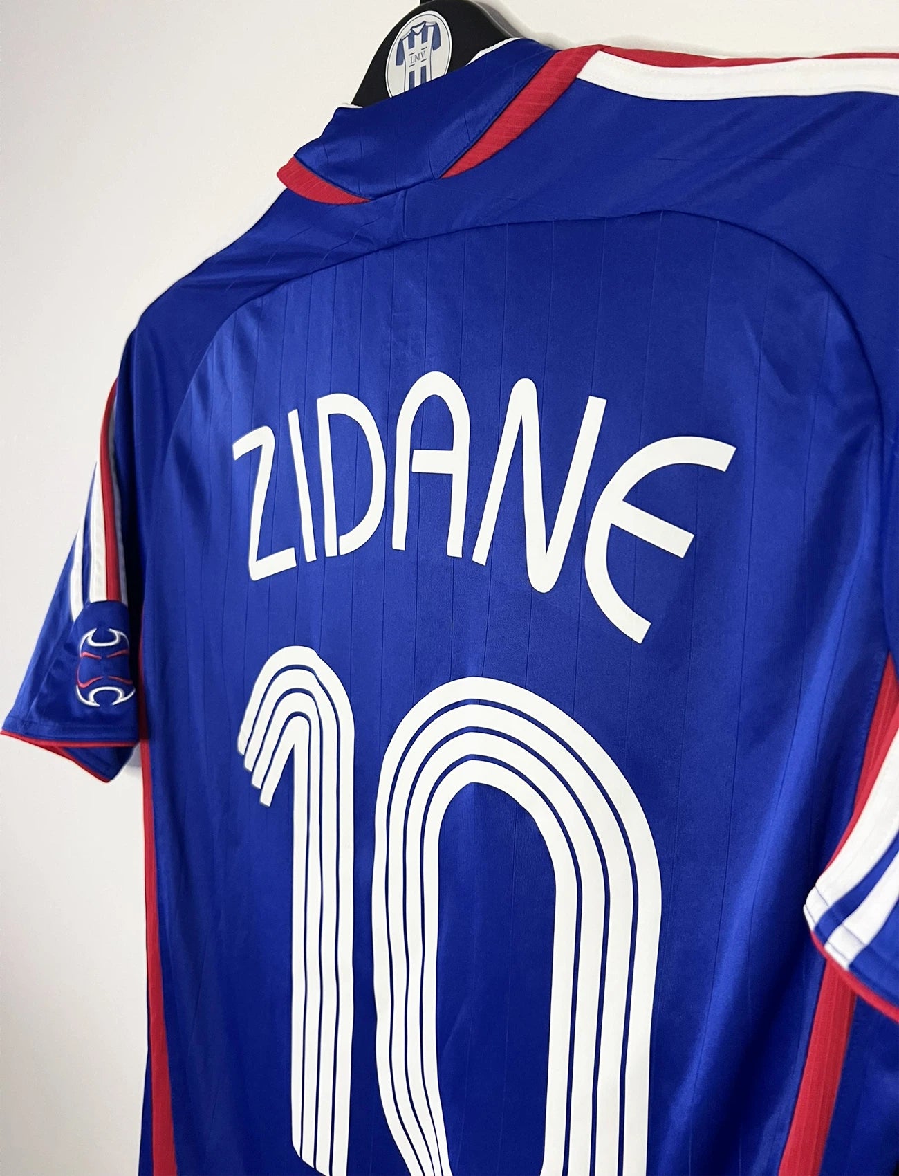 Maillot de foot vintage domicile bleu de l'équipe de france 2006. On peut retrouver l'équipementier Adidas. Le maillot est floqué du numéro 10 Zinedine Zidane. Il s'agit d'un maillot authentique d'époque comportant l'étiquette 740126.