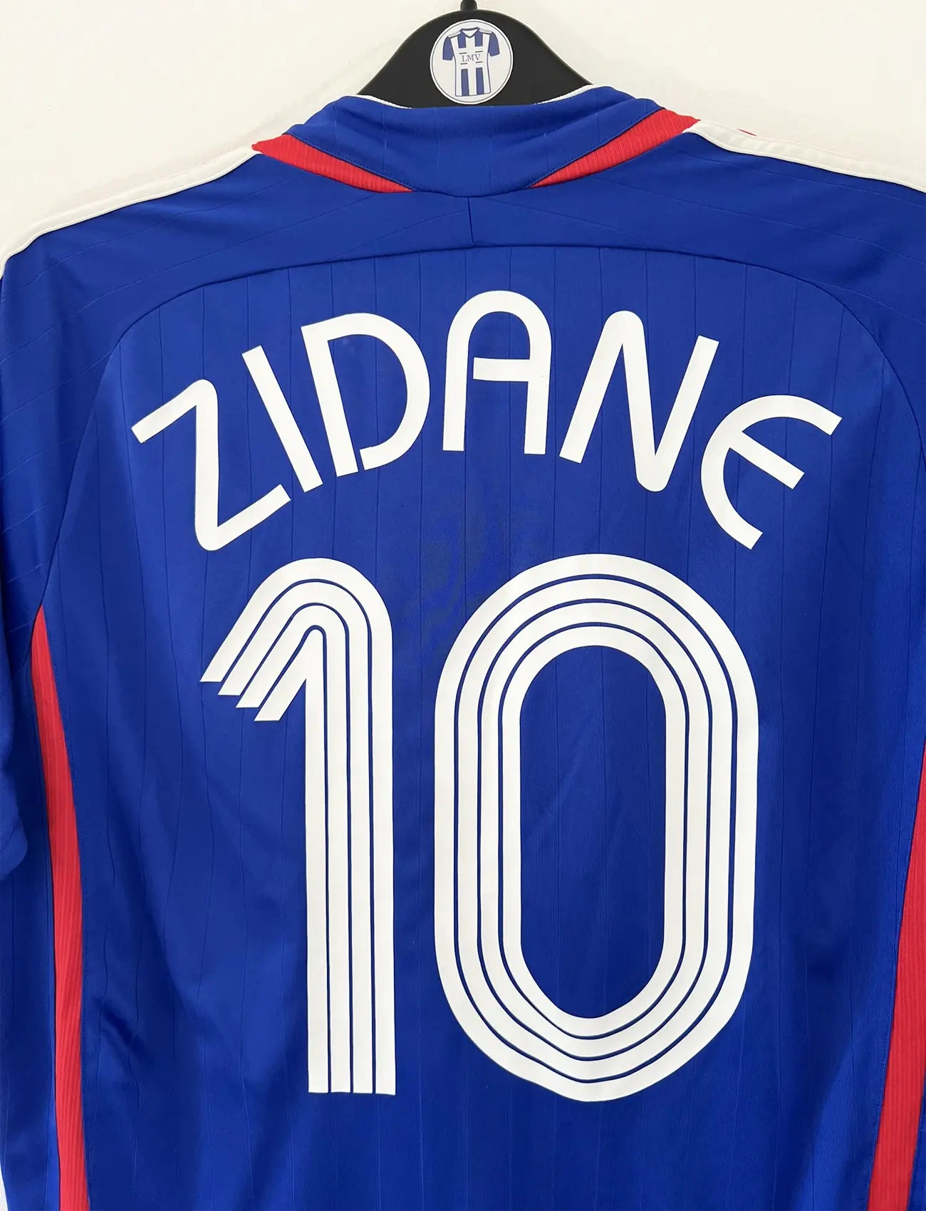 Maillot de foot vintage domicile bleu, blanc et rouge de l'équipe de france 2006. On peut retrouver l'équipementier adidas. Le maillot est floqué du numéro 10 Zinedine Zidane. Il s'agit d'un maillot authentique d'époque comportant l'étiquette 740126