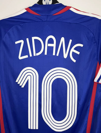 Maillot de foot vintage domicile bleu de l'équipe de france 2006. On peut retrouver l'équipementier Adidas. Le maillot est floqué du numéro 10 Zinedine Zidane. Il s'agit d'un maillot authentique d'époque comportant l'étiquette 740126.