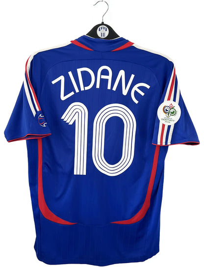 Maillot de foot vintage domicile bleu, blanc et rouge de l'équipe de france 2006. On peut retrouver l'équipementier adidas. Le maillot est floqué du numéro 10 Zinedine Zidane. Il s'agit d'un maillot authentique d'époque comportant l'étiquette 740126