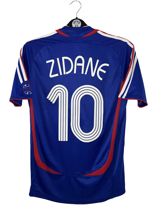 Maillot de foot vintage domicile bleu de l'équipe de france 2006. On peut retrouver l'équipementier Adidas. Le maillot est floqué du numéro 10 Zinedine Zidane. Il s'agit d'un maillot authentique d'époque comportant l'étiquette 740126.