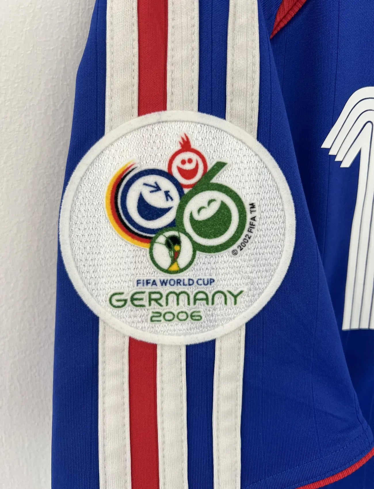 Maillot de foot vintage domicile bleu, blanc et rouge de l'équipe de france 2006. On peut retrouver l'équipementier adidas. Le maillot est floqué du numéro 10 Zinedine Zidane. Il s'agit d'un maillot authentique d'époque comportant l'étiquette 740126