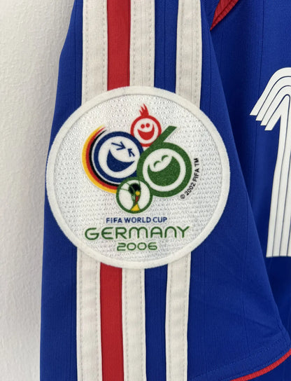 Maillot de foot vintage domicile bleu, blanc et rouge de l'équipe de france 2006. On peut retrouver l'équipementier adidas. Le maillot est floqué du numéro 10 Zinedine Zidane. Il s'agit d'un maillot authentique d'époque comportant l'étiquette 740126