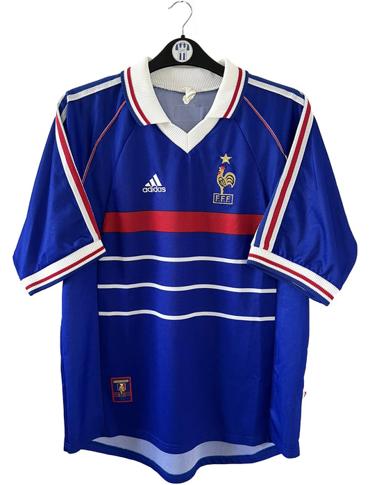 Maillot de foot vintage domicile bleu, blanc et rouge de l'équipe de france 1998. On peut retrouver l'équipementier adidas. Le maillot est floqué du numéro 17 Emmaunel Petit. Il s'agit d'un maillot authentique d'époque