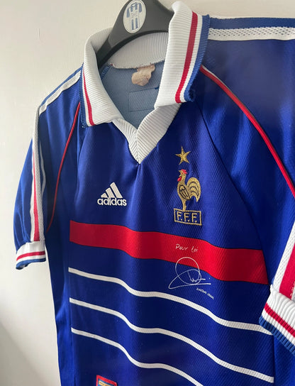 Maillot foot vintage domicile equipe de france 1998 bleu blanc et rouge. On peut retrouver l'équipementier adidas. Il s'agit d'un maillot authentique d'époque. Le maillot est floqué du numéro 10 Zinedine Zidane et comporte également sa signature avec la mention "pour toi Zinedine Zidane"