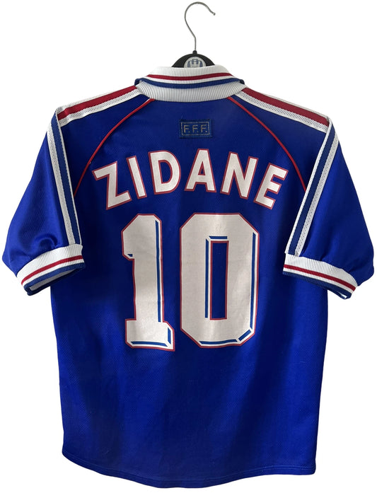 Maillot foot vintage domicile equipe de france 1998 bleu blanc et rouge. On peut retrouver l'équipementier adidas. Il s'agit d'un maillot authentique d'époque. Le maillot est floqué du numéro 10 Zinedine Zidane et comporte également sa signature avec la mention "pour toi Zinedine Zidane"