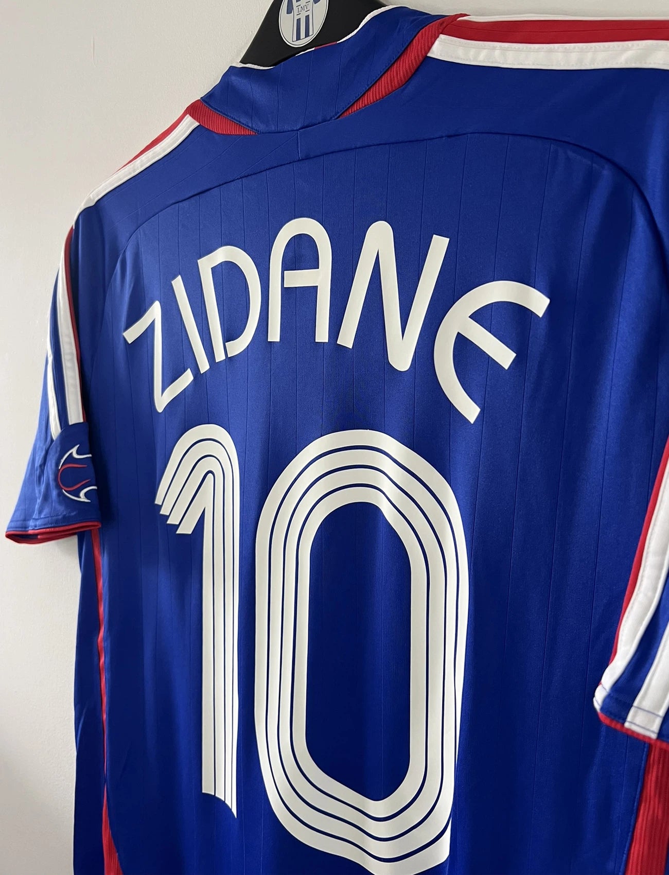 Maillot de foot vintage domicile bleu de l'équipe de france 2006. On peut retrouver l'équipementier adidas. Le maillot est floqué du numéro 10 Zinedine Zidane. Il s'agit d'un maillot authentique comportant l'étiquette 740126.