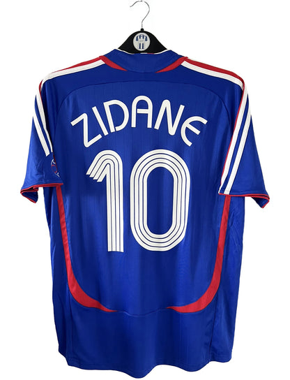 Maillot de foot vintage domicile bleu de l'équipe de france 2006. On peut retrouver l'équipementier adidas. Le maillot est floqué du numéro 10 Zinedine Zidane. Il s'agit d'un maillot authentique comportant l'étiquette 740126.