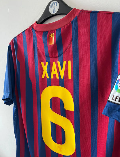 Maillot de foot vintage domicile rouge et bleu du FC Barcelone 2011/2012. On peut retrouver l'équipementier Nike et le sponsor Qatar Foundation. Le maillot est floqué du numéro 6 Xavi. Il s'agit d'un maillot authentique d'époque.