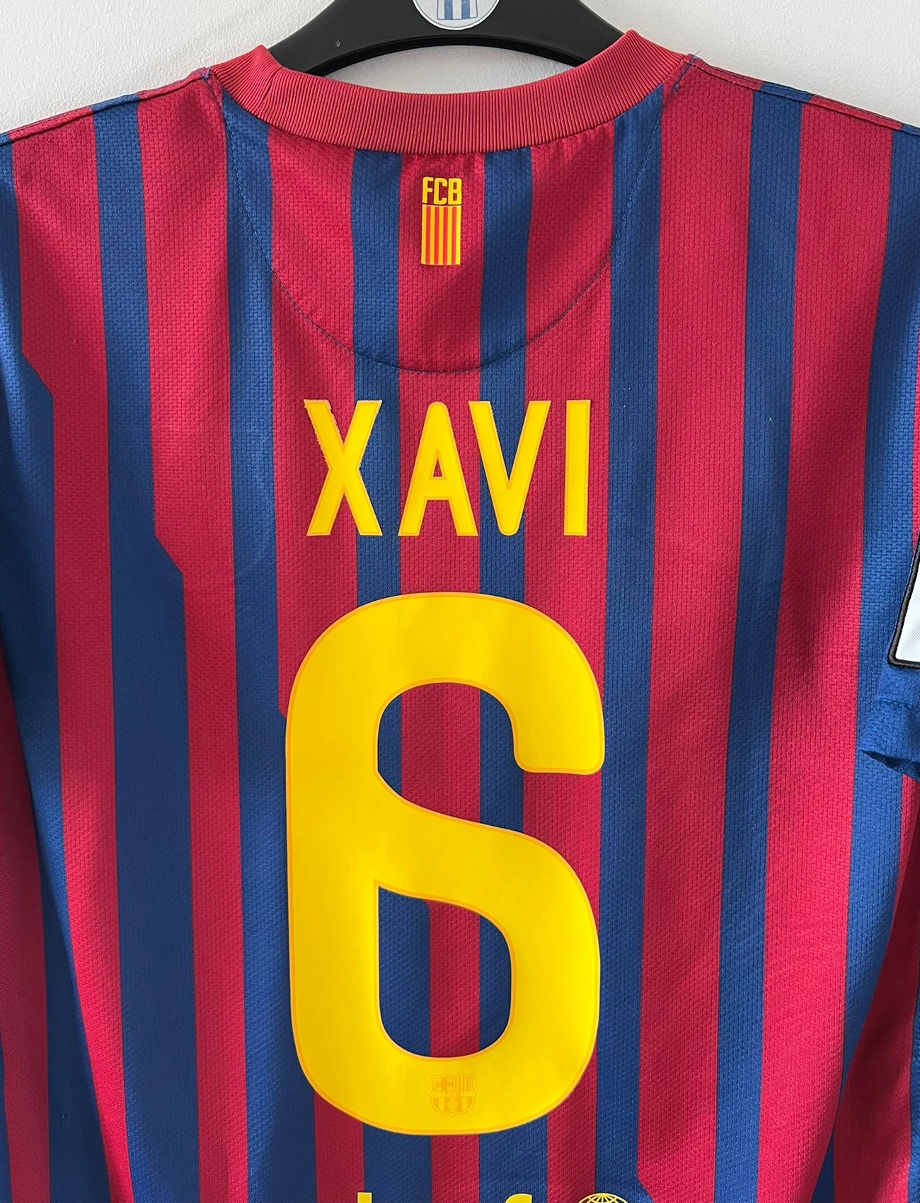 Maillot de foot vintage domicile rouge et bleu du FC Barcelone 2011/2012. On peut retrouver l'équipementier Nike et le sponsor Qatar Foundation. Le maillot est floqué du numéro 6 Xavi. Il s'agit d'un maillot authentique d'époque.