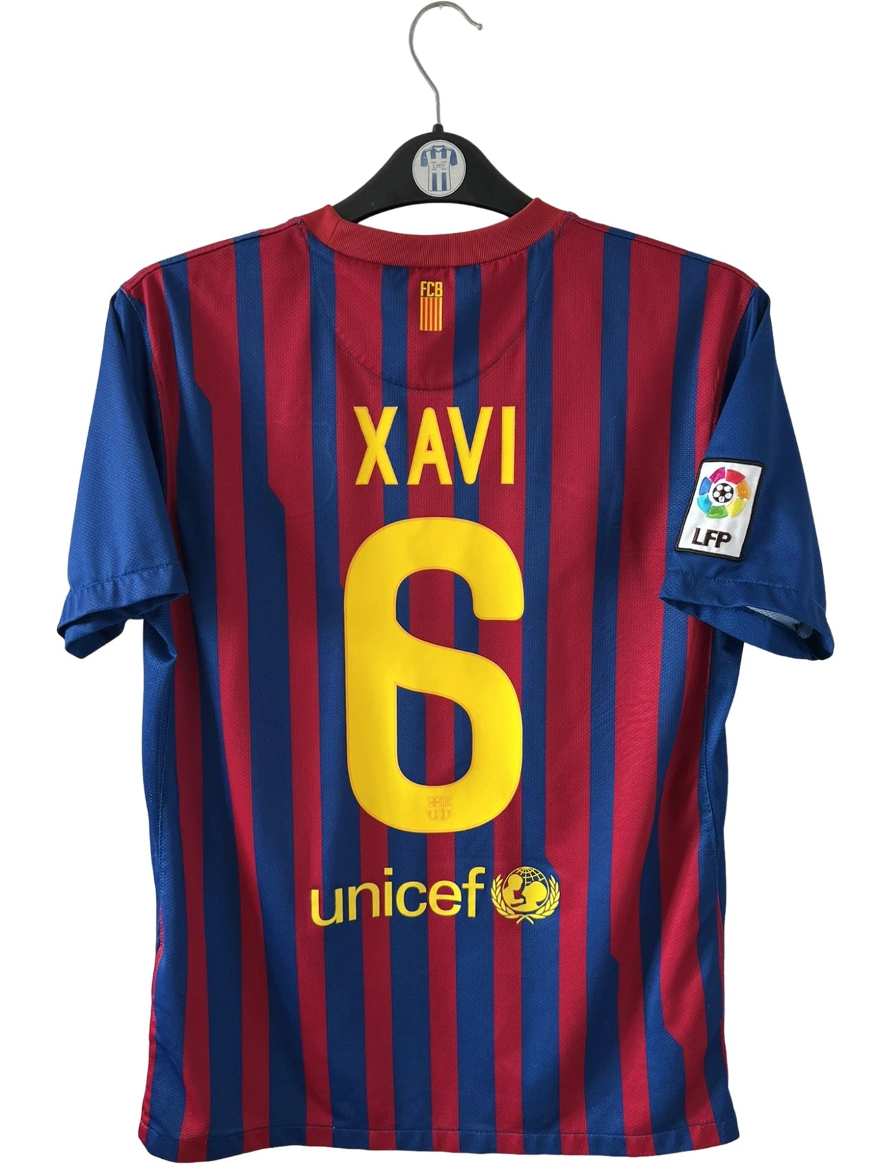 Maillot de foot vintage domicile rouge et bleu du FC Barcelone 2011/2012. On peut retrouver l'équipementier Nike et le sponsor Qatar Foundation. Le maillot est floqué du numéro 6 Xavi. Il s'agit d'un maillot authentique d'époque.