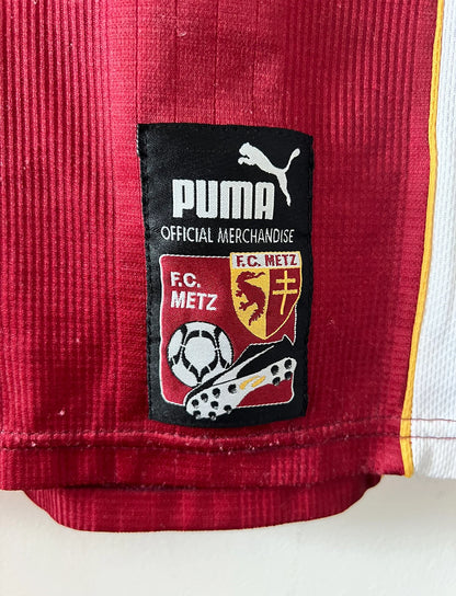 Maillot de foot vintage domicile rouge et blanc du FC Metz de la saison 1998/1999. On peut retrouver l'équipementier Puma et le sponsor Sollac. Le maillot est floqué du numéro 14 Geoffray Toyes. Il s'agit d'un maillot authentique d'époque.