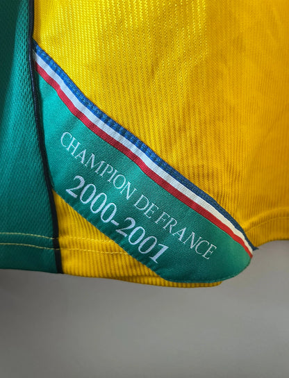 Maillot foot vintage domicile jaune et vert du FC Nantes 2001/2002. On peut retrouver l'équipementier Le Coq Sportif et le sponsor Synergie. Il s'agit d'un maillot authentique d'époque.
