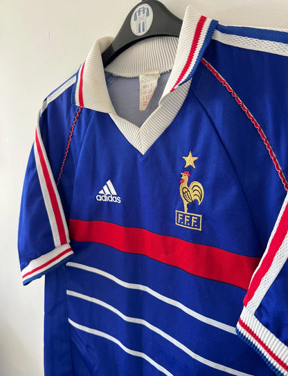 Maillot de foot vintage domicile bleu de l'équipe de France 1998. On peut retrouver l'équipementier Adidas. Il s'agit d'un maillot authentique d'époque.