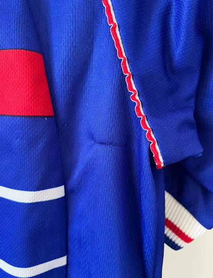 Maillot de foot vintage domicile bleu de l'équipe de France 1998. On peut retrouver l'équipementier Adidas. Il s'agit d'un maillot authentique d'époque.