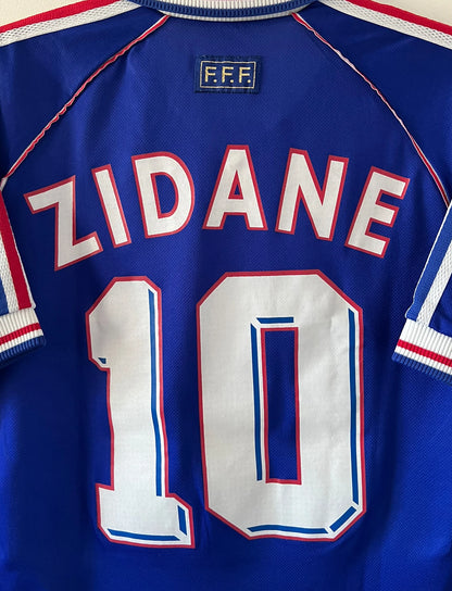 Maillot foot vintage domicile equipe de france 1998 bleu blanc et rouge. On peut retrouver l'équipementier adidas. Le maillot est floqué du numéro 10 Zinedine Zidane. Il s'agit d'un maillot authentique d'époque avec la signature de Zidane en sérigraphié.