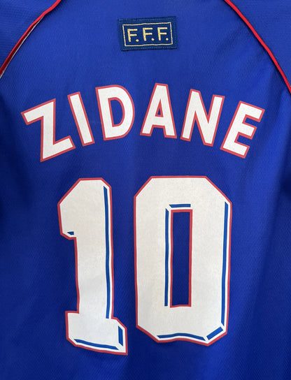 Maillot de foot vintage domicile de l'équipe de france 1998 bleu. On peut retrouver l'équipementier adidas. Le maillot est floqué du numéro 10 Zinedine Zidane. Il s'agit d'un maillot authentique d'époque.