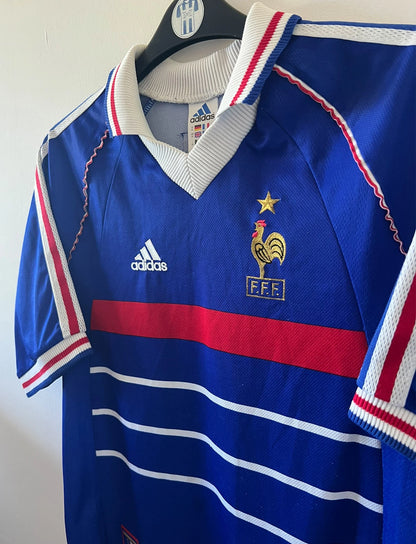 Maillot de foot vintage domicile bleu de l'équipe de france 1998. On peut retrouver l'équipementier Adidas. Le maillot est floqué du numéro 10 Zinedine Zidane. Il s'agit d'un maillot authentique d'époque.