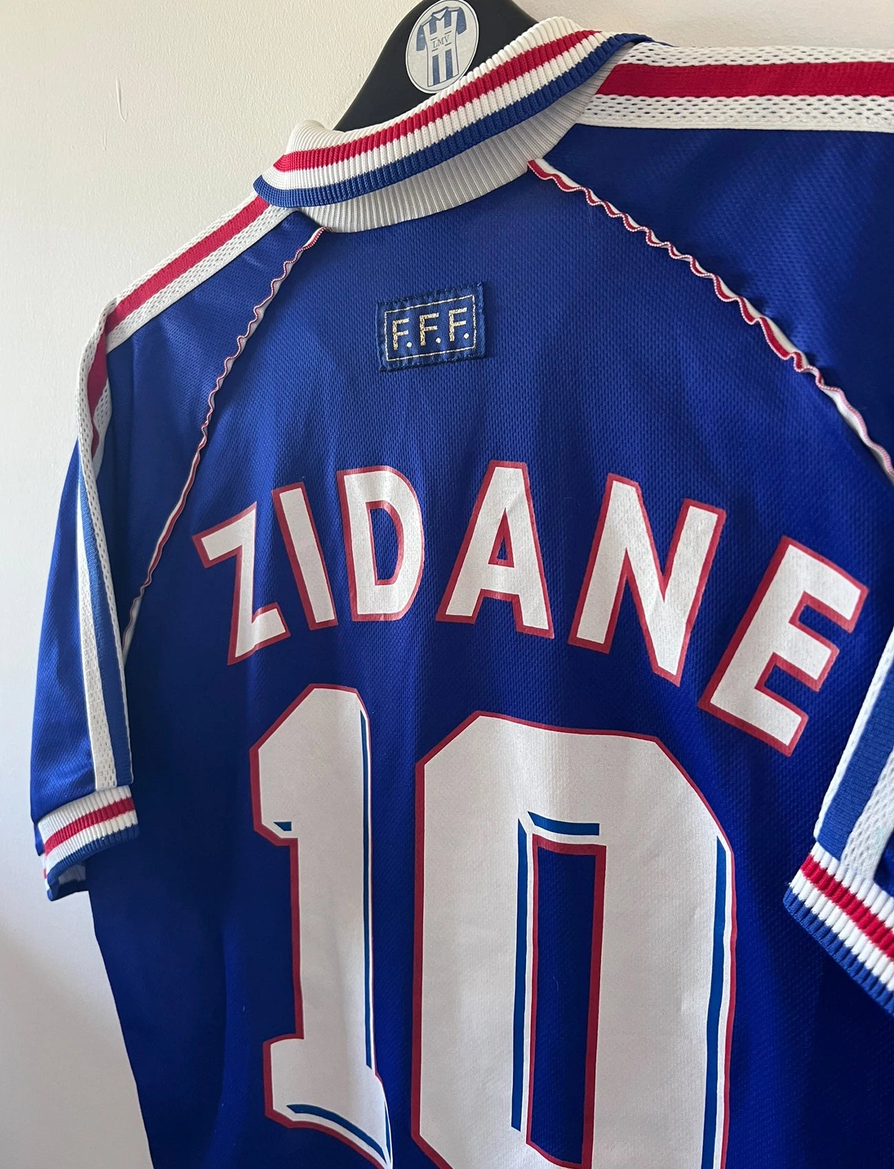 Maillot de foot vintage domicile bleu de l'équipe de france 1998. On peut retrouver l'équipementier Adidas. Le maillot est floqué du numéro 10 Zinedine Zidane. Il s'agit d'un maillot authentique d'époque.