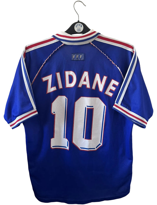 Maillot de foot vintage domicile bleu de l'équipe de france 1998. On peut retrouver l'équipementier Adidas. Le maillot est floqué du numéro 10 Zinedine Zidane. Il s'agit d'un maillot authentique d'époque.