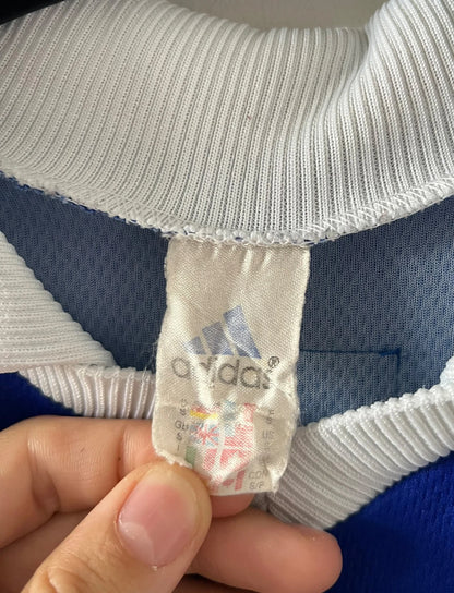 Maillot de foot vintage domicile bleu de l'équipe de france 1998. On peut retrouver l'équipementier Adidas. Le maillot est floqué du numéro 10 Zinedine Zidane. Il s'agit d'un maillot authentique d'époque.