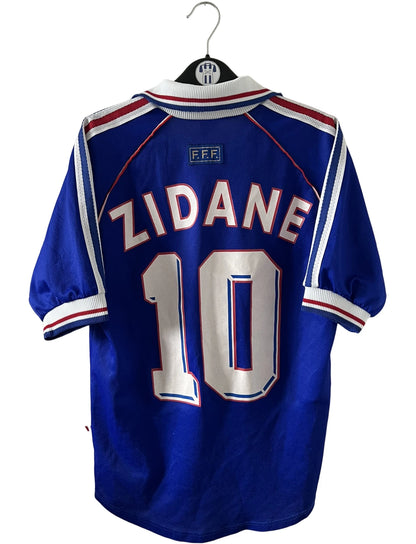 Maillot de foot vintage domicile bleu de l'équipe de france 1998. On peut retrouver l'équipementier Adidas. Le maillot est floqué du numéro 10 Zinedine Zidane. Il s'agit d'un maillot authentique d'époque.