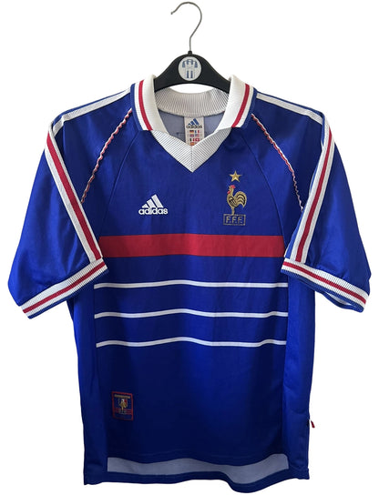Maillot de foot vintage domicile bleu de l'équipe de france 1998. On peut retrouver l'équipementier Adidas. Le maillot est floqué du numéro 10 Zinedine Zidane. Il s'agit d'un maillot authentique d'époque.