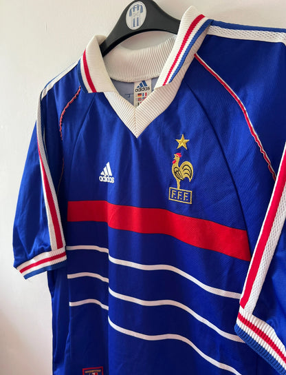 Maillot de foot vintage domicile bleu de l'équipe de France 1998. On peut retrouver l'équipementier Adidas. Le maillot est floqué du numéro 10 Zinedine Zidane. Il s'agit d'un maillot authentique d'époque.