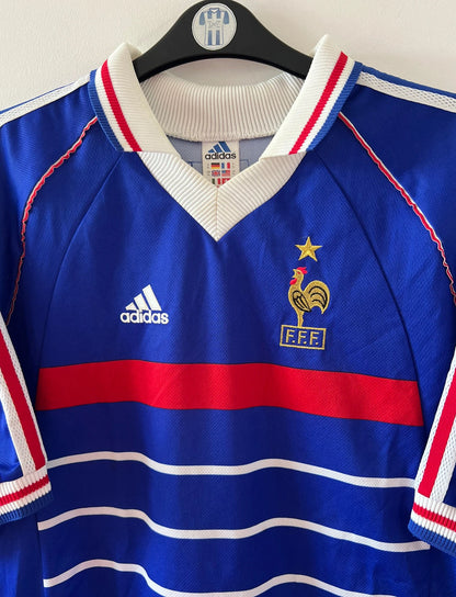 Maillot de foot vintage domicile bleu de l'équipe de France 1998. On peut retrouver l'équipementier Adidas. Le maillot est floqué du numéro 10 Zinedine Zidane. Il s'agit d'un maillot authentique d'époque.