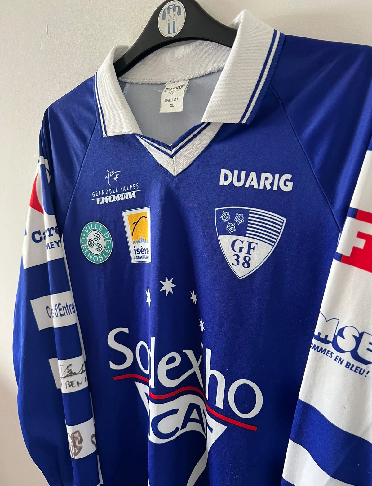 Maillot de foot vintage domicile bleu et blanc de Grenoble de la saison 1999/2000. On peut retrouver l'équipementier Duarig et l'équipementier Sodexho. Il s'agit d'un maillot authentique d'époque.